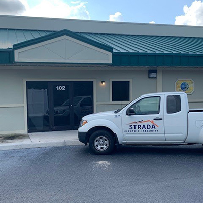 A white Strada Services pickup truck is parked in front of a building.