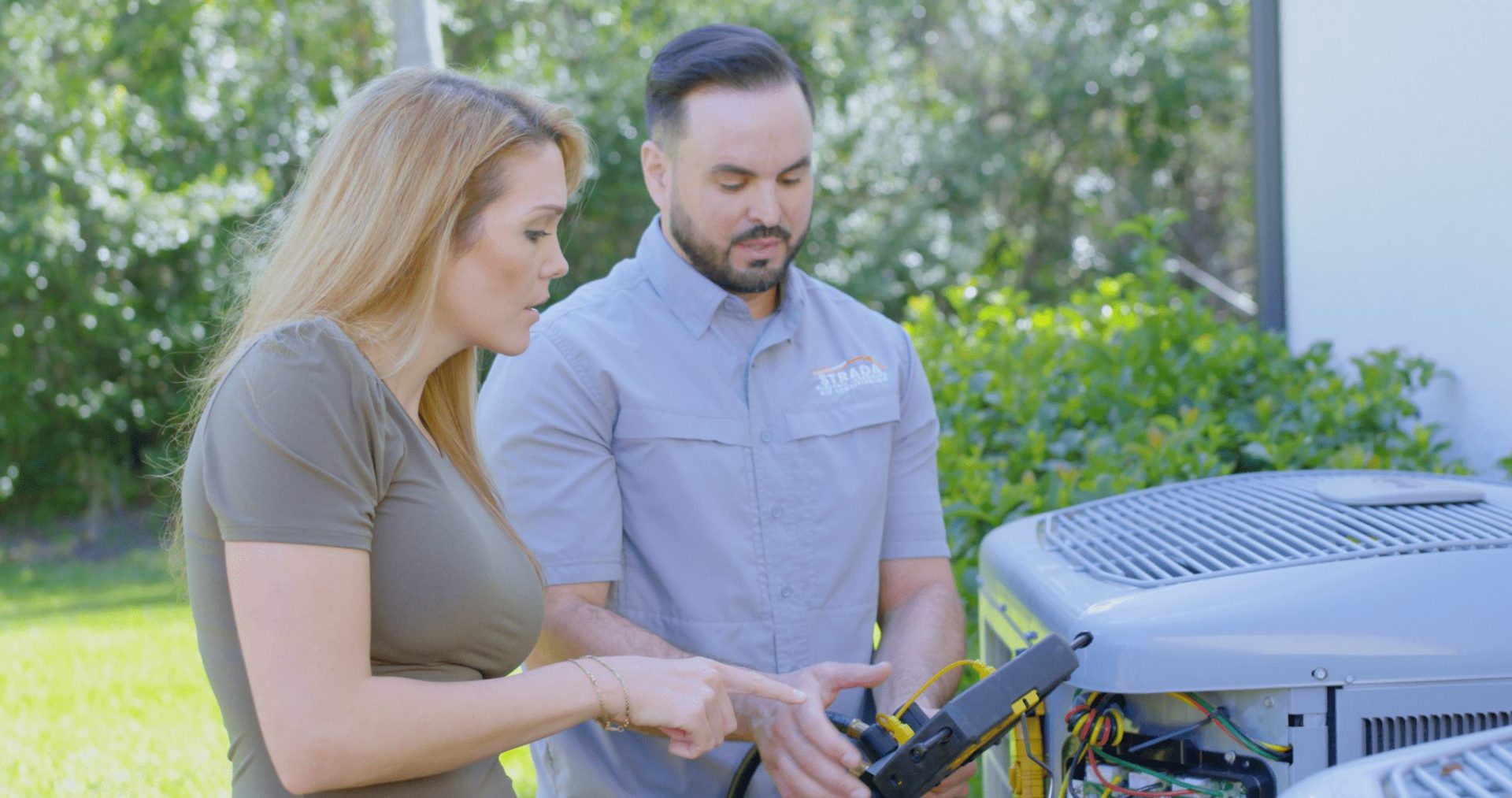 Strada Services technician working on HVAC system outside and talking with homeowner