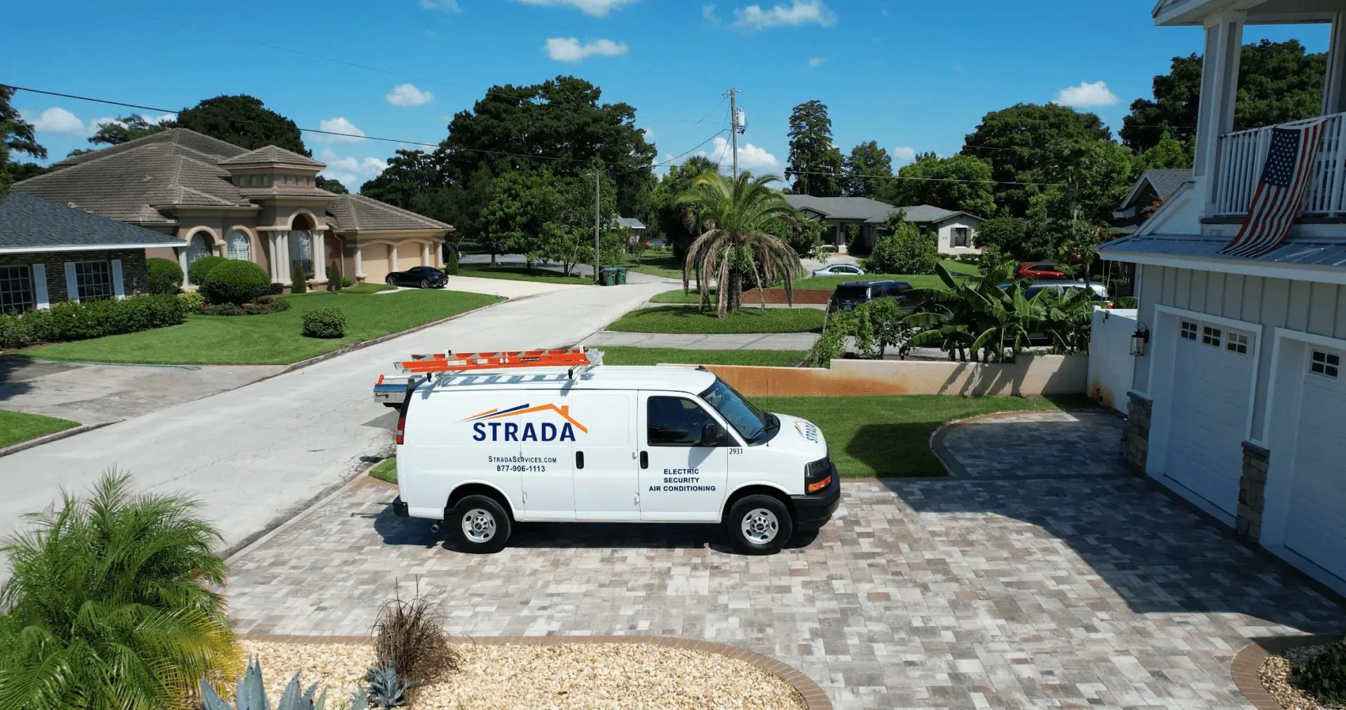 A white Strada Services utility van with an orange ladder on the roof is parked in a driveway.