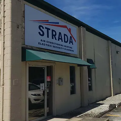 Vista lateral de un edificio. Un cartel sobre la puerta de entrada dice &quot;Strada Air Conditioning Heating Electric Security plomería&quot;.