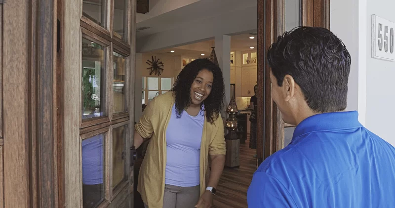 Una mujer mantiene abierta la puerta de su casa y sonríe a un empleado de Strada Services vestido con un polo azul.
