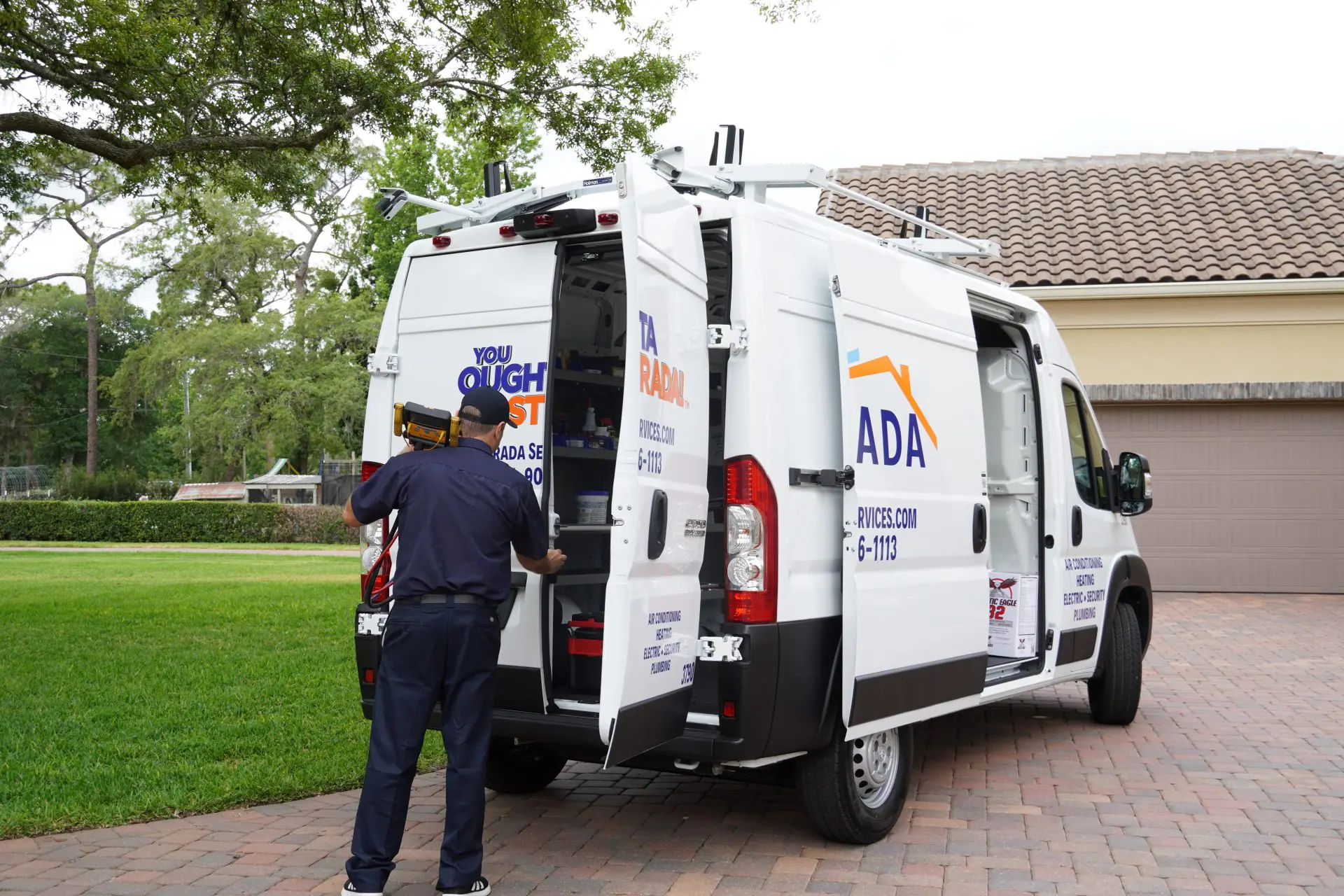 A white Strada Services utility van has a red ladder on the roof. The van reads, "Electric, Security, Air Conditioning".