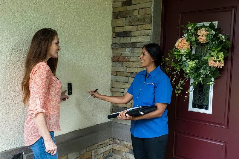 A woman and a female Strada Services employee are standing in front a home security system at the woman's front door.