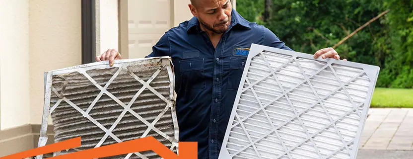 Professional HVAC inspector holding a new, clean HVAC filter and a dirty, broken HVAC filter.